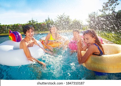 Teenage boys and girls with inflatable rings splash in swimming pool playing together - Powered by Shutterstock