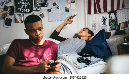 Teenage boys hanging out in a bedroom playing a video game and using a smartphone - Powered by Shutterstock