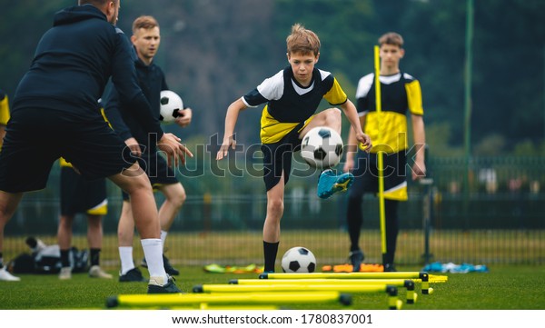 2人の若いコーチとのサッカーの練習会で10代の男の子 練習中にボールを蹴るジュニアレベルのサッカー選手 サッカーの訓練は ハードルの敏捷さで訓練される の写真素材 今すぐ編集