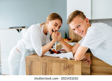 Teenage brother and her adult sister, young in 20s, arm wrestling at cozy home kitchen. - Shutterstock ID 2021431010