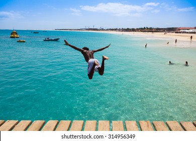 Teenage Cape Verdean Boy Jumping On The Turquoise  Water Of Santa Maria Beach In Sal Cape Verde - Cabo Verde