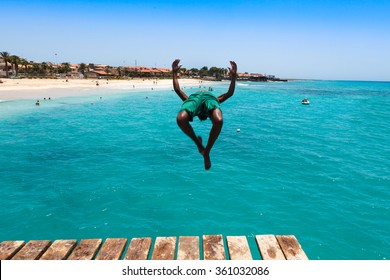 Teenage Cape Verdean Boy Jumping On The Turquoise  Water Of Santa Maria Beach In Sal Cape Verde - Cabo Verde