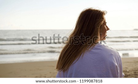 Teenage caucasian girl with brown hair looking at the Pacific Ocean from behind.
