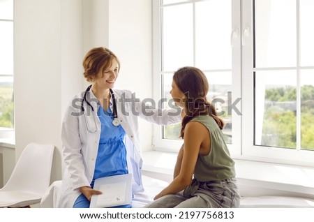 Teenage child visits friendly doctor. Cheerful, positive pediatrician in white coat smiles and puts her hand on shoulder of happy school girl. Healthcare, medical checkup, trust, and support concept