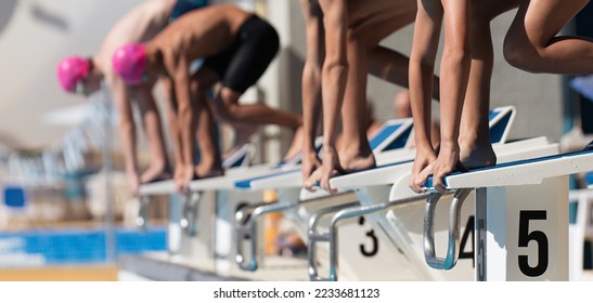 Teenage children on the starting blocks ready to dive into the pool at the beginning of a swimming race - Powered by Shutterstock