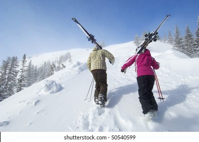 Teenage Couple (16-17) Holding Skis, Hiking Up Slope, Back View.