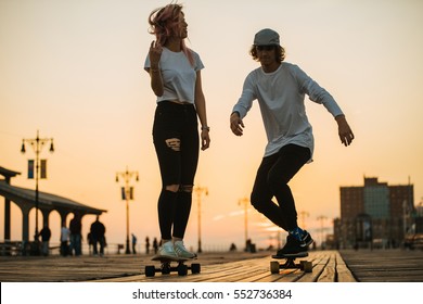 Teenage couple riding longboards on the boardwalk