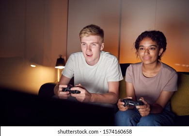 Teenage Couple Sitting On Sofa At Home Computer Gaming Together