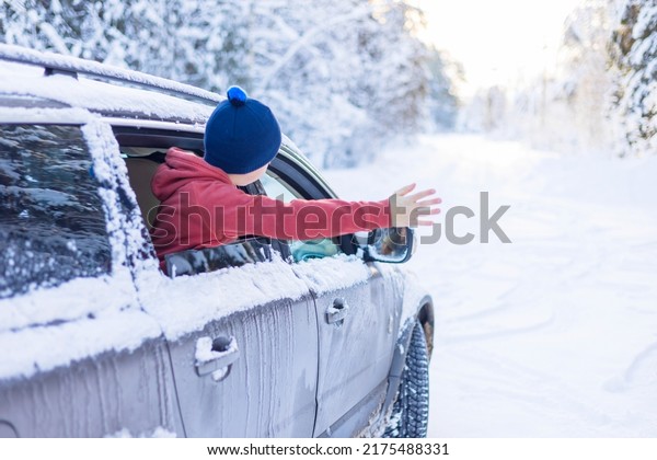 teenage cute\
boy in sweater, vest and white knitted hat in car window in snowy\
forest having fun, concept of winter local travel during Christmas\
or New Year holidays and\
vacations