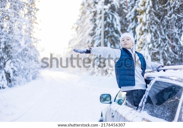 teenage cute\
boy in white sweater, vest and white knitted hat in car window in\
snowy forest having fun, concept of winter local travel during\
Christmas or New Year holidays and\
vacations