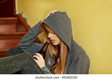 Teenage depressed woman sitting on the staircase and drinking a beer