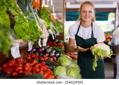 Teenage Female Seller In Uniform Working In Supermarket At Her First Job, Showing Cauliflower