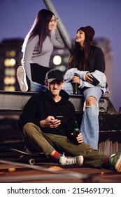 Teenage Friends Chilling With Bottles Of Beer At Roof Party At Night.