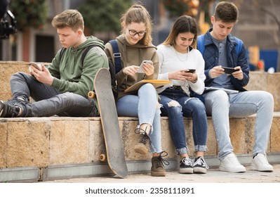 Teenage friends spending time together using smartphones outdoors - Powered by Shutterstock