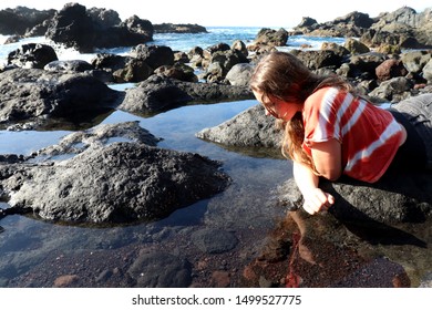 Teenage girl (13) looks down into the clear water of a natural pool at low tide on a rocky beach in the 
Atlantic Ocean in Los Gigantes, Spain on the island of Tenerife in the Canary Islands. 