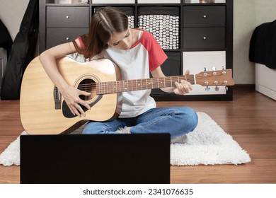 A teenage girl with an acoustic guitar and laptop, enjoying her passion for music in her room  - Shutterstock ID 2341076635