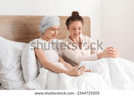 Teenage girl after chemotherapy and her sister using tablet computer in bedroom