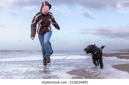 A teenage girl and a black dog labradoodle are running in shallow water on the beach of Haarlem Amsterdam, Netherlands, Januay 2022 - Powered by Shutterstock