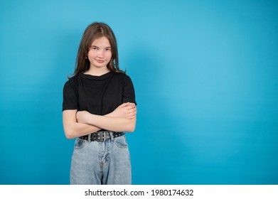 A Teenage Girl In A Black T-shirt Stands With Arms Crossed On Her Chest. Awkward Age Concept. High Quality Photo