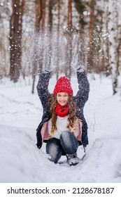 A teenage girl in bright clothes laughs and throws snow up. Outdoor games during the cold season. Beautiful nature. Vertical photo of children.