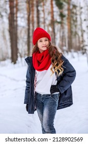 A teenage girl in bright clothes poses against the backdrop of a pine forest. The girl looks away and smiles. Walk in nature in the cold season. Beautiful nature. Vertical photo of children.
