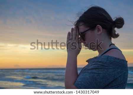 Teenage girl with brown hair praying at sunset on a beautiful beach