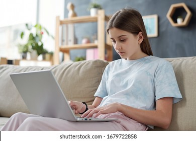 Teenage girl in casualwear sitting on couch with laptop on her knees while browsing in the net in home environment - Shutterstock ID 1679722858