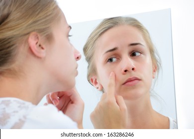Teenage girl checking her face for pimple in the mirror