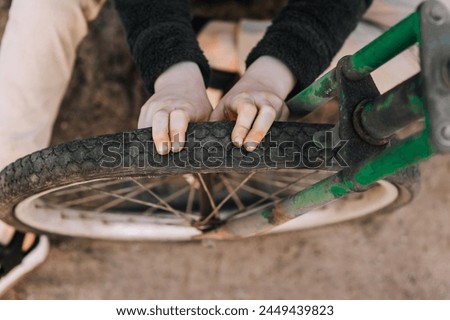 Teenage girl, child sitting near a rusty old retro bicycle with a broken, punctured wheel outdoors, pressing her hands on the tire. Close-up photography, portrait, lifestyle.