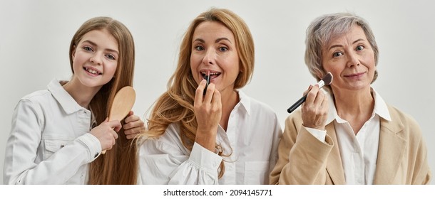 Teenage girl combing hair while her mother painting lips with lipstick and grandmother doing makeup with cosmetic brush. Age and generation concept. Caucasian family of three female generations