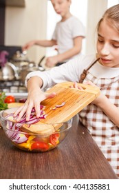 Teenage girl cooking together with her family in the kitchen Caucasian girl putting onion into mixing bowl with salad Family cooking background