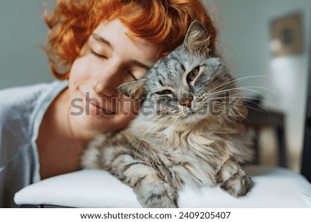 teenage girl with curly red hair, with pet, large gray striped fluffy cat, spends time together.