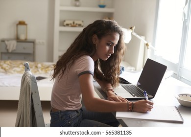 Teenage girl doing homework at a desk in her bedroom - Shutterstock ID 565381135