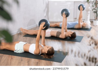 Teenage girl doing pilates exercises with soft ball in female group in studio