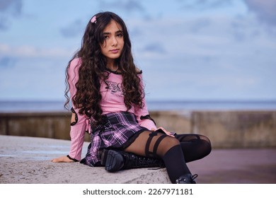 Teenage girl dressed in gothic style sitting on a wall facing the sea - Shutterstock ID 2267971181