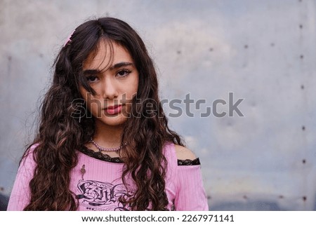 Teenage girl dressed in gothic style posing standing in front of a metal gate