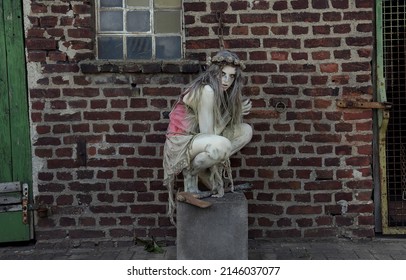 A Teenage Girl Is Dressed In Rags As A Halloween Horror 
Figure. She Sits On A Cement Block With A Sinister Look
On Her Face. A Rusty Old Axe Is By Her Side. 