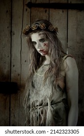 A teenage girl dresses as a Halloween horror figure. 
Her face and body are covered with filth and blood
as she peers into the camera. She wears a thorny floral
crown on her head. 