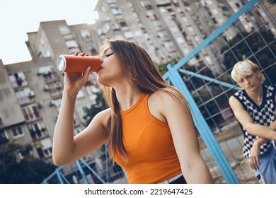 A teenage girl drinks soda on a street.