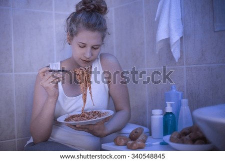 Teenage girl eating spaghetti in bathroom