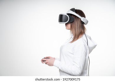 Teenage girl with fair hair is playing game with a gamepad and VR glasses in a white studio, glasses covers almost all her face, side view, waist high - Powered by Shutterstock