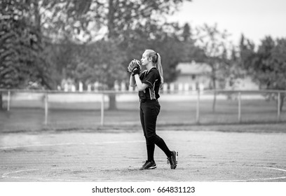 A teenage girl in fast ball pitching stance on the pitchers mound in uniform in black and white - Powered by Shutterstock