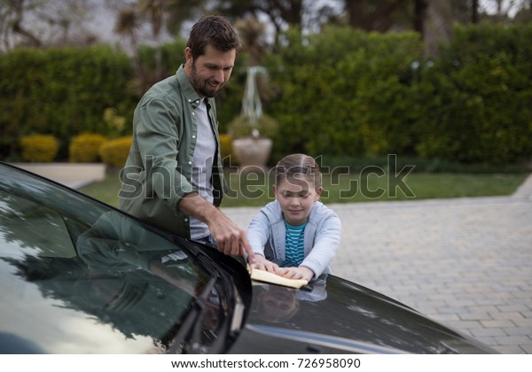 Teenage girl\
and father washing a car on a sunny\
day