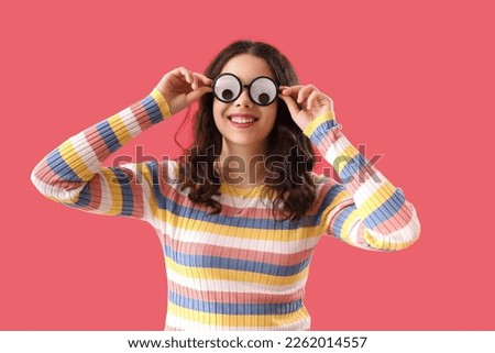 Teenage girl in funny eyeglasses on red background. April Fools' Day celebration