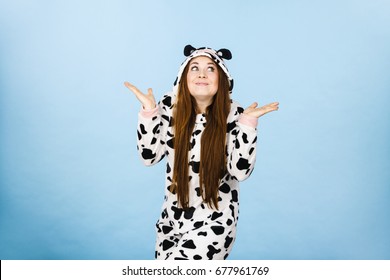 Teenage girl in funny nightclothes, pajamas cartoon style making silly face, shrugging woman in doubt doing shrug, confused girl gesturing do not know sign, studio shot on blue.