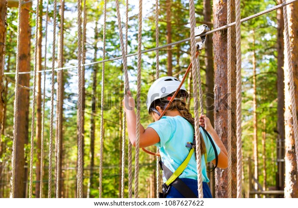 Teenage girl goes on hinged trail in extreme rope\
Park in summer forest. High-altitude climbing training of child on\
adventure track, equipped with safety straps and protective helmet.\
Estonian summer