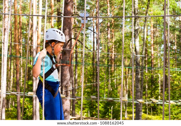 Teenage girl goes on hinged trail in extreme rope\
Park in summer forest. High-altitude climbing training of child on\
adventure track, equipped with safety straps and protective helmet.\
Estonian summer