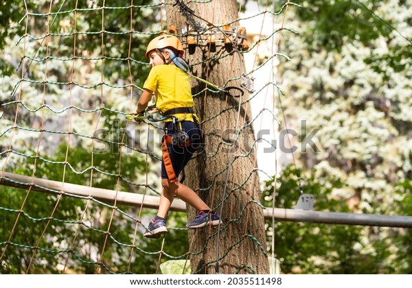 Teenage\
girl goes on hinged trail in extreme rope Park in summer forest.\
High-altitude climbing training of child on adventure track,\
equipped with safety straps and protective\
helmet