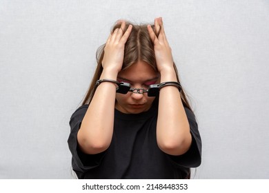 A Teenage Girl In Handcuffs Hides Her Face On A Gray Background. Juvenile Delinquent In A Black T-shirt, Criminal Liability Of Minors.