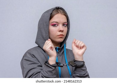 A Teenage Girl In Handcuffs On A Gray Background. Juvenile Delinquent, Criminal Liability Of Minors. Members Of Youth Criminal Groups And Gangs.